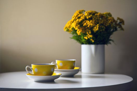 Yellow dotted retro cups and yellow chrysanthemum flowers on white table. Vintage teaset