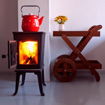 red kettle boiling on a retro stove in the kitchen. open fireplace. Focus on a spout. country home design with furnace at the interior