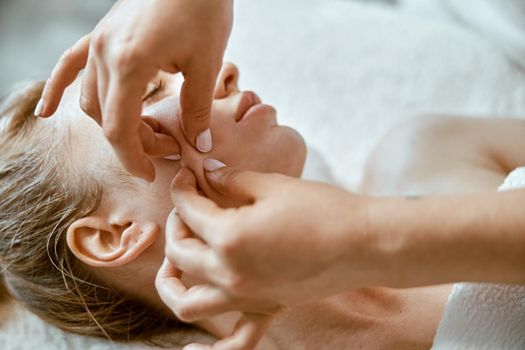 Therapist is doing face relaxing massage to a young woman in modern wellness cabinet