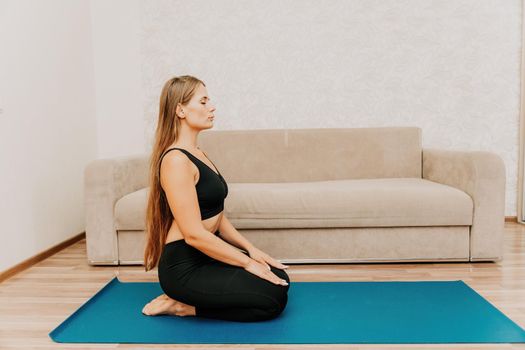 Young woman with long hair, fitness instructor in black sportswear, doing stretching and pilates on yoga mat at home. Female fitness yoga routine concept. Healthy lifestyle harmony and meditation