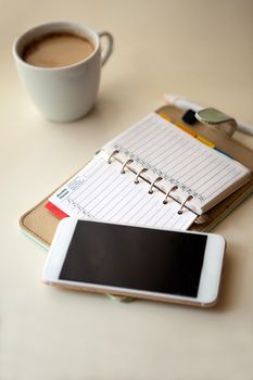 Day planner noter with Mobile phone and notes paper. cozy working place at home. stylish interior in warm pastel colors, table and white coffee mug with glasses. stay at home - a place for home office