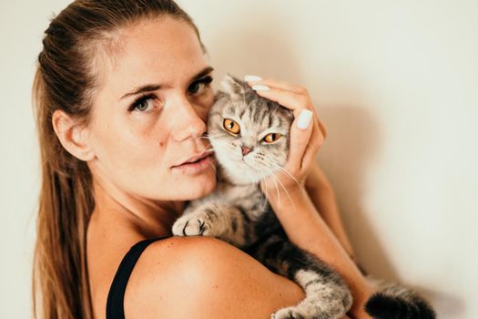 Attractive girl embracing her pet with smile. Indoor portrait of cute ginger woman playing with cat.