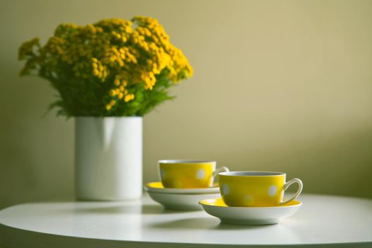 Yellow dotted retro cups and yellow chrysanthemum flowers on white table. Vintage teaset