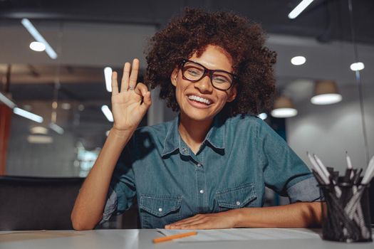 Smiling Afro American lady in glasses communicating in sign language while looking at camera