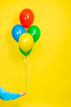 Female hand hold a bunch of colorful balloons. Party or present concept. Green, red, yellow, and blue Balloons and hand isolated on yellow backgroun.