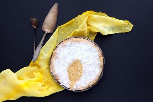 bundt cake on a black background with yellow blanket and retrospoons. Homemade pie on a dark backdrop and powdered sugar spoon shadow. bundt cake on a black background with yellow blanket and retrospoons.