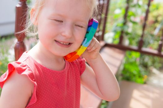 Cute caucasian fair hair girl in pink dress is playing and showing funny trendy silicone antistress colorful toy popit. Push Popper fidget toy is the ideal toy to get rid of your frustration or stress.