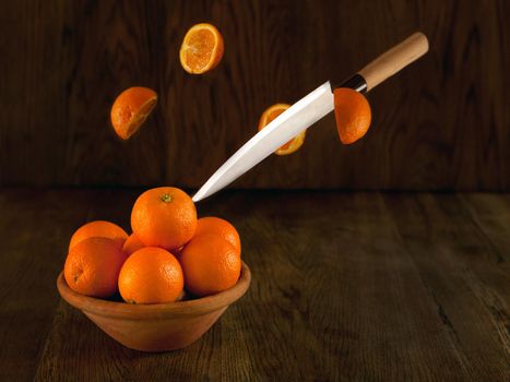 Knife cutting oranges. A lot of oranges on the bowl - dark background. Still life fruits in vintage style. Flying tasty oranges at the bowl dark photo. action and movement
