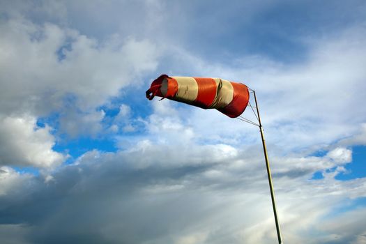 Red and white windsock blows against a blue sky. Meteorology wind bag for marine navigation