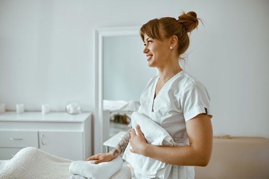 beautiful happy caucasian female masseur is posing in white minimalistic modern treatment salon