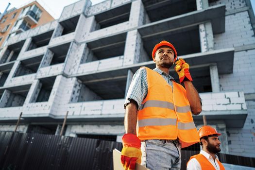 Young construction worker in uniform using walkie talkie on site, close up portrait