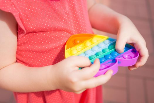 Children's hands hold a silicone toy. Push Popper fidget toy is the ideal toy to get rid of your frustration or stress. Kid having fun with popular simple dimple multicolored rainbow colors toy. Kids being kids LGBTQ colors Vertical. Summer vibes. Outdoor Outside.