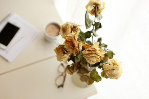 old roses at the working table as procrastination or delay or exhaustion concept. vintage style - glasses, note book with pencil pen and coffee mug on the table