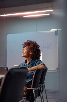 Happy female worker sitting at the table in the meeting room and holding mobile phone