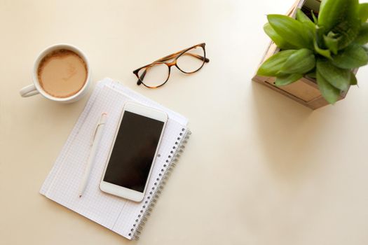 Mobile phone and notes paper. Retro style interior - cozy working place at home stylish interior in warm pastel colors, table and white coffee mug with glasses. stay at home - a place for home office or a place to relax.