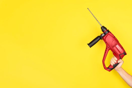 Red Puncher in the hands of a builder. Female hand hold new Puncher or drill isolated on yellow background. Banner with copy space