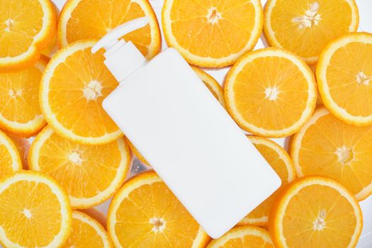 white cream bottle with a dispenser without a label on a background of sliced oranges, face and body cream with the addition of orange oil concept, mock up