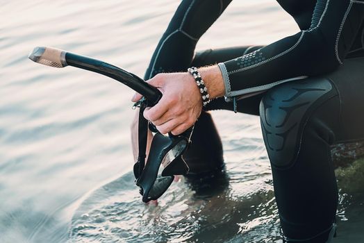 Unrecognizable diver man holding snorkel and mask on background of sea, closeup of hand