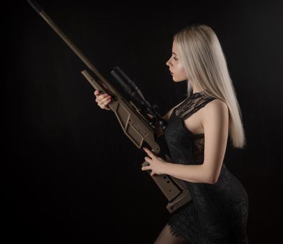 the young blonde girl in black dress posing on black background with weapon