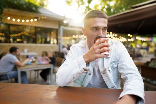 Young man with cup of coffee sitting in outdoor cafe, close up