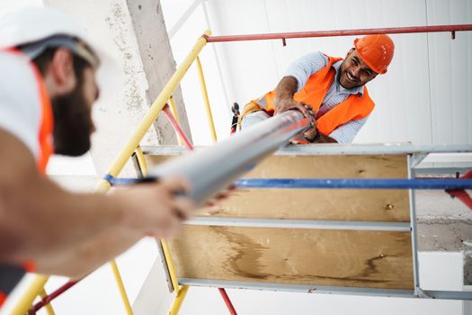 Two men builder in work uniform drag the pipe on scaffolding at construction site