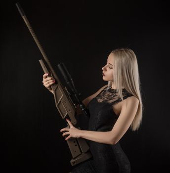 the young blonde girl in black dress posing on black background with weapon