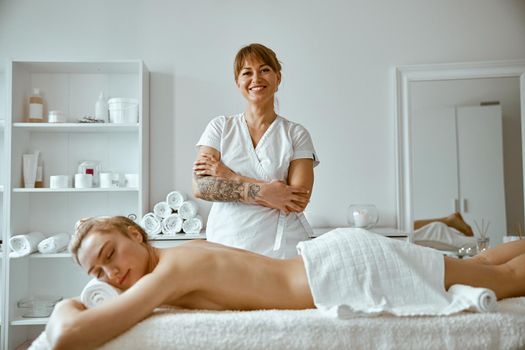 confident female specialist is doing relaxing body massage for beautyful slim caucasian lady at minimalistic spa salon