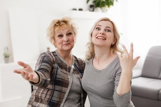 Self portrait of pretty charming positive funky mother and daughter shooting selfie on front camera having video-call sitting in modern white living room enjoying meeting free time