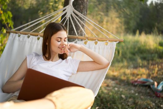 cheerful woman lies in a hammock with a laptop vacation internet travel. High quality photo