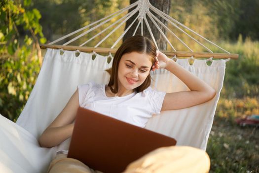 cheerful woman lies in a hammock with a laptop vacation internet travel. High quality photo