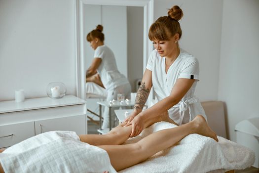Professional caucasian specialist is doing leg message at modern minimalistic salon