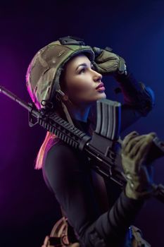 the woman in a military airsoft uniform with an American automatic rifle and a helmet on a dark background
