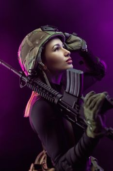 the woman in a military airsoft uniform with an American automatic rifle and a helmet on a dark background