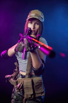 the woman in a military airsoft uniform in a vest with an American automatic rifle on a dark background