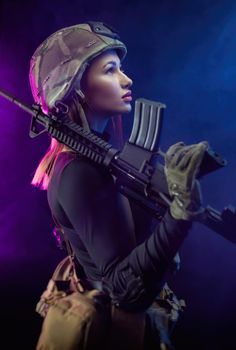 the woman in a military airsoft uniform with an American automatic rifle and a helmet on a dark background