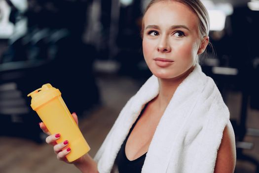 Young sporty woman having a drink in a gym after workout, close up