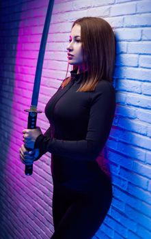 the sexy slender woman in black clothes with a katana in her hand in neon light