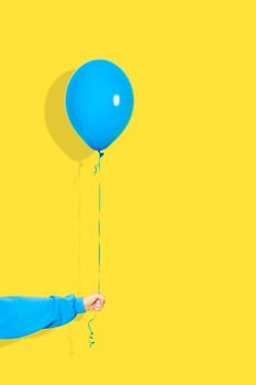 Female hand hold blue balloon. Party or present concept. Blue Balloon and hand in blue hoodie isolated on yellow backgroun.