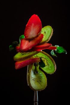 Sliced fresh and juicy green kiwi and red strawberry on the silver fork on dark background. healthy food concept. close up. low key. 2