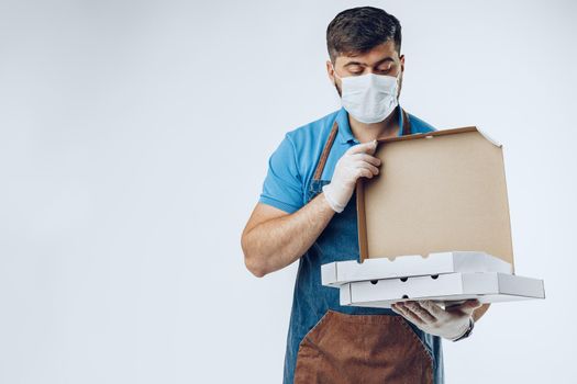 Pizza delivery man in medical gloves and mask against grey background. Safe service while coronavirus covid-19 outbreak