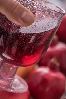 Hand with a glass of pomegranate juice on with fresh pomegranate fruits background. Side close up.