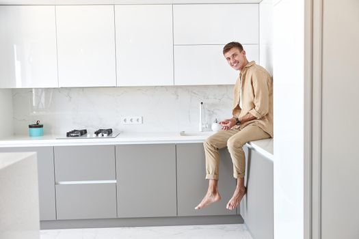 Happy handsome man is standing on minimalistic kitchen and smiling