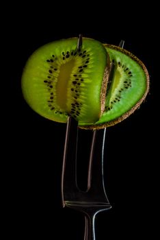 Sliced fresh and juicy green kiwi on the silver fork on dark background. healthy food concept. close up. low key. 3