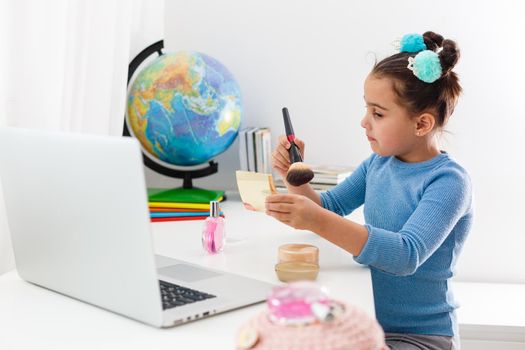 little girl learning make up powder, brush, blush on laptop online, distance learning