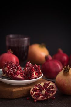 A glass of pomegranate juice with fresh pomegranate fruits and seeds on wooden rustic background. Side view. Low key