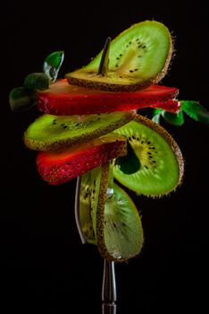 Sliced fresh and juicy green kiwi and red strawberry on the silver fork on dark background. healthy food concept. close up. low key.6