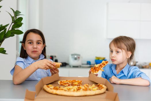 Two happy little child girl friends eating pizza slices.