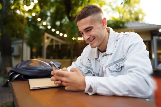 Young man using smartphone while sitting at outdoor cafe, close up