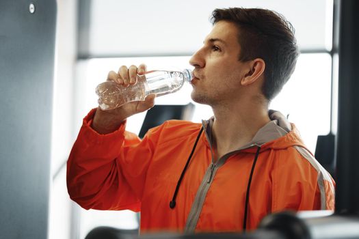 Portrait of young man drinking some water from a bottle in a gym, close up