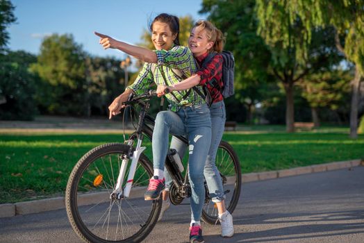 Two pretty young caucasian girls searching the way on a bicycle along the street. Best friends enjoying a day on a bike. Sunny summer evening.